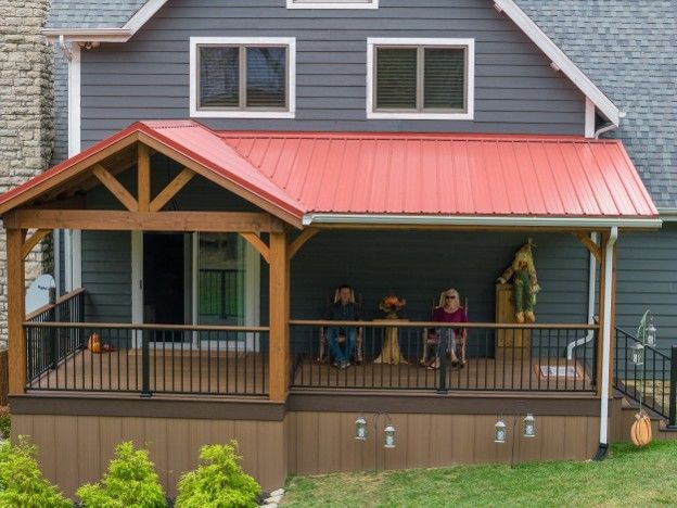 Covered porch on a blue house with red roof, railings, and small figures standing outside.