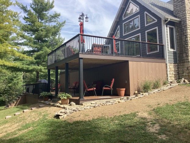 Modern cabin with a raised deck, red chairs, and stone siding on a grassy slope.