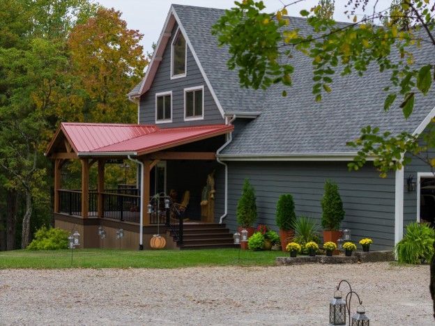 Dark gray house with red porch roof and fall foliage, viewed from a gravel driveway