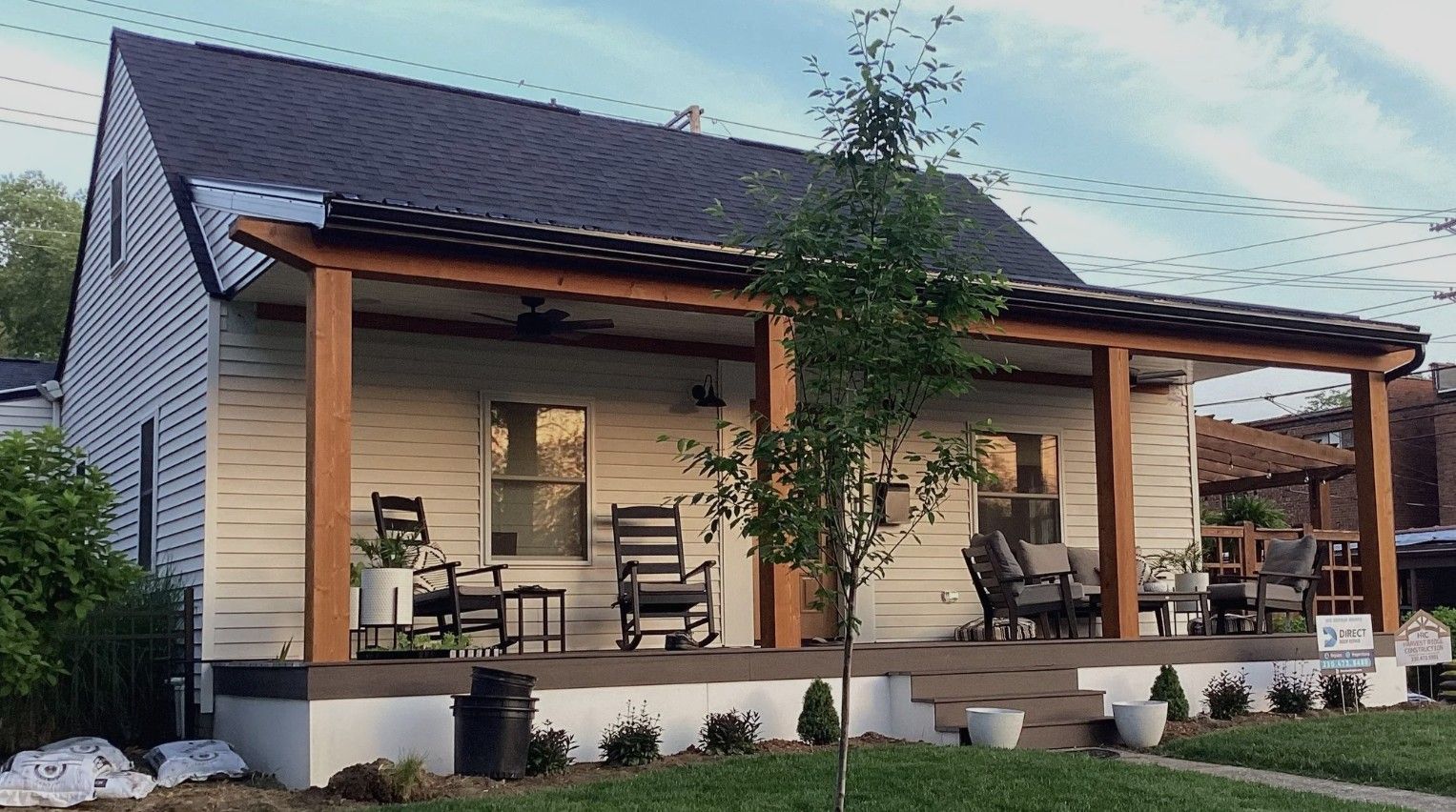 Modern house with a covered wooden porch, chairs, potted plants, and a sloped roof at dusk.
