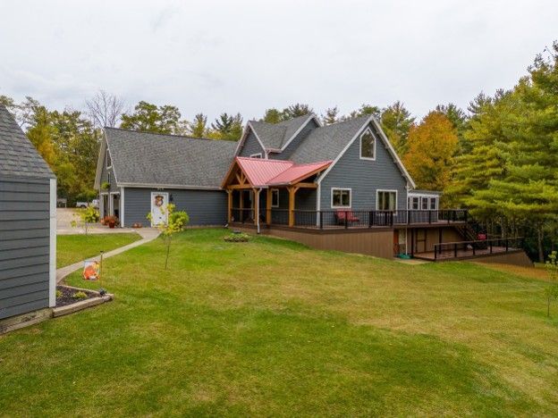 Gray house with red-roofed porch and large lawn, surrounded by trees