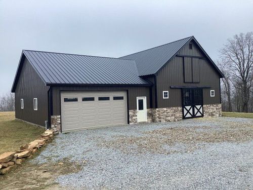 Gray barn-style house with attached garage and gravel driveway on a rural lot