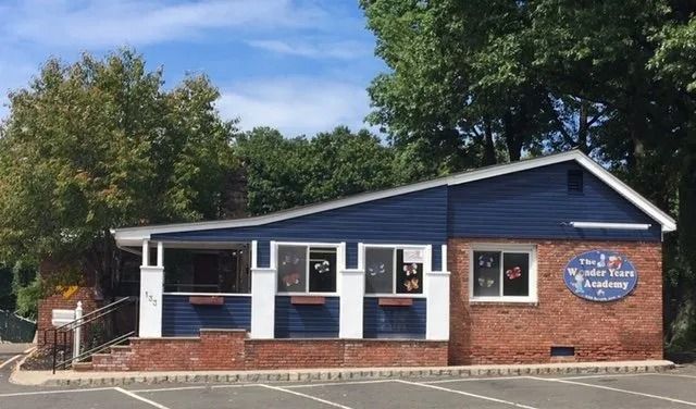 Small blue-and-red brick storefront with white trim and a round sign, viewed from the street.