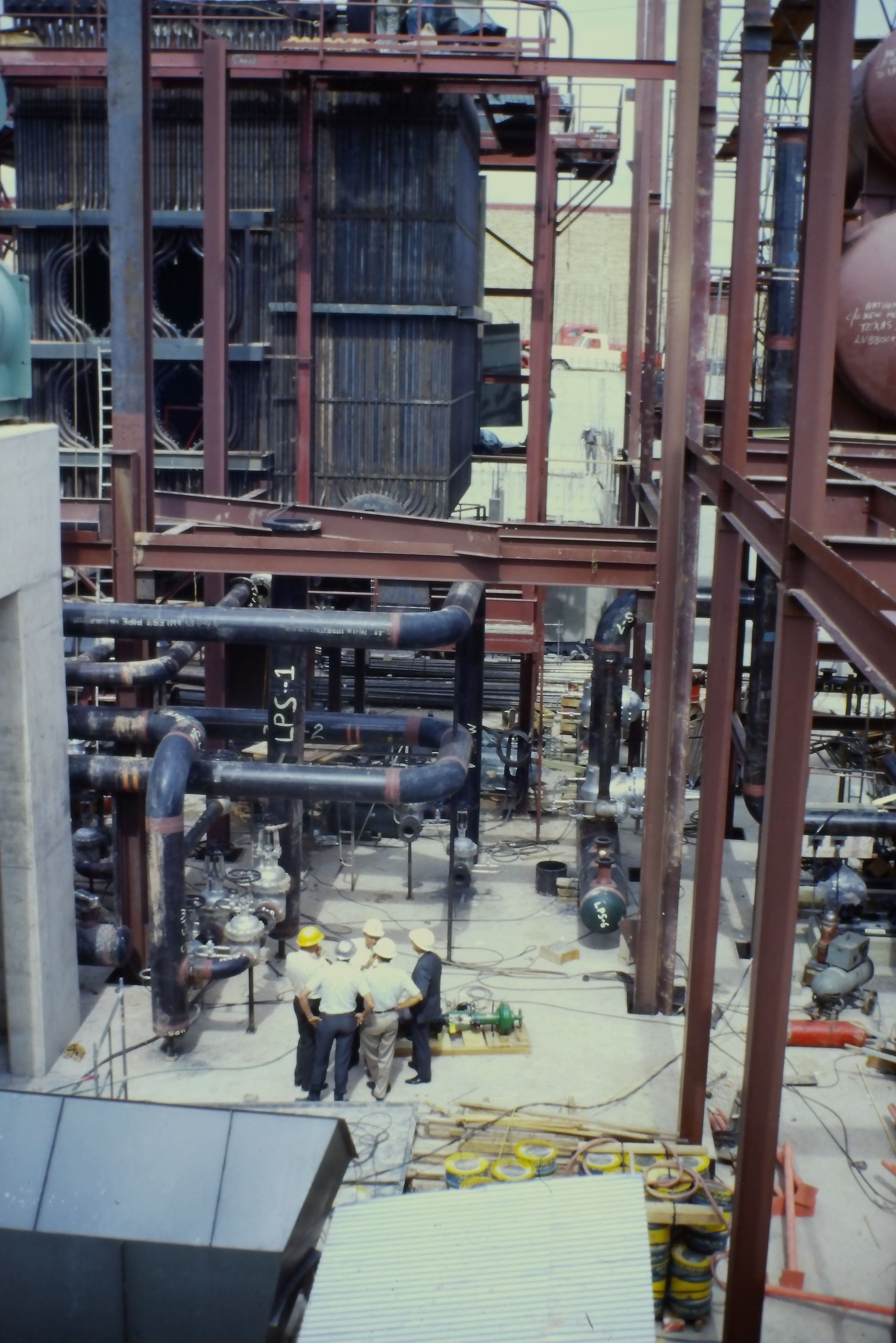A group of men are standing in front of a building with pipes and a sign that says 5