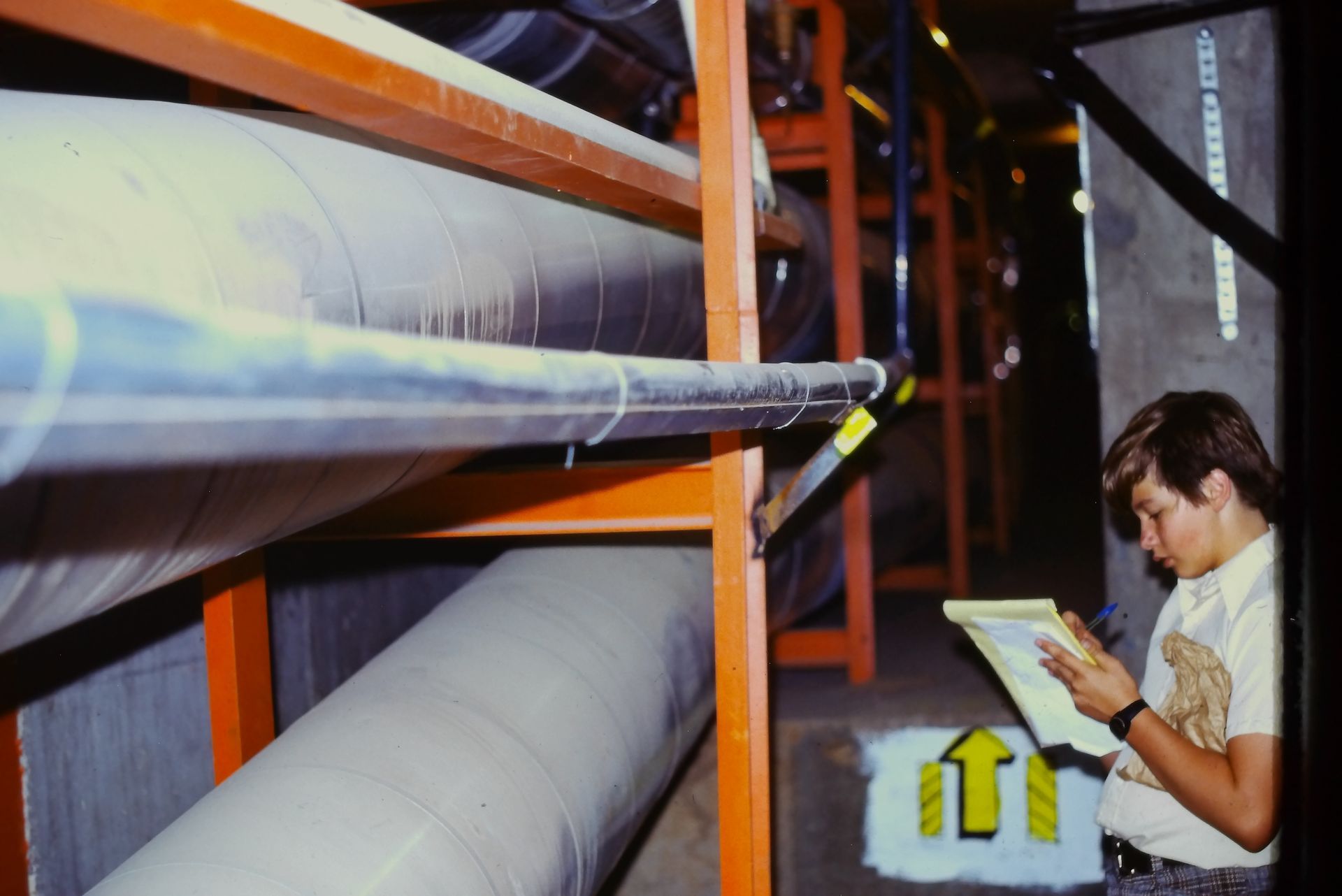 A man is looking at a clipboard in a room with pipes