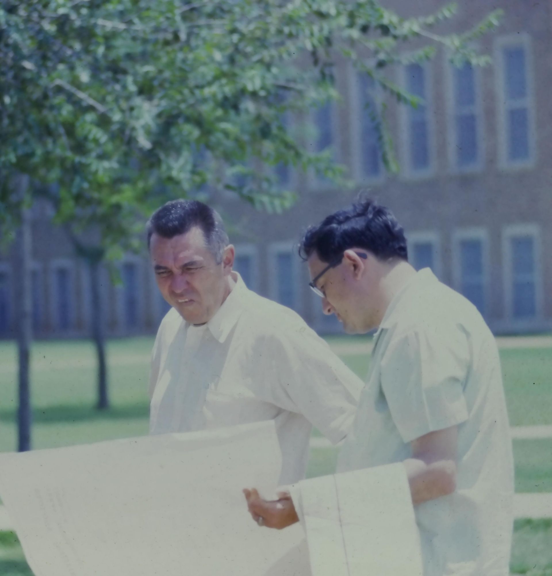 Two men are looking at a large piece of paper in front of a building.