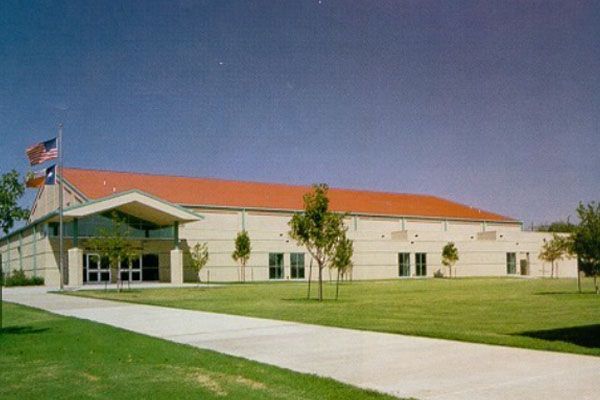 A large white building with a red roof is surrounded by grass and trees.