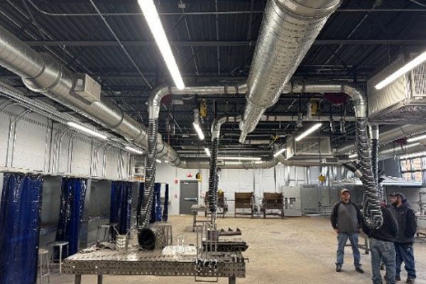 A group of men are standing in a large room with a lot of pipes hanging from the ceiling.