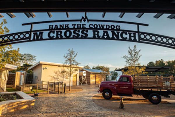 A red truck is parked under a sign that says hank the cowdog m cross ranch