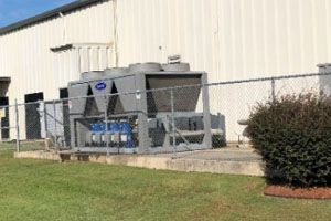 A large machine is sitting in front of a building behind a chain link fence.