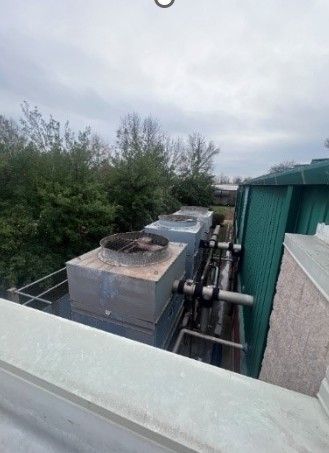 A rooftop view of a building with a lot of pipes and trees in the background.