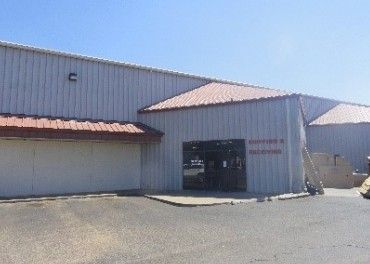 A large white building with a red roof is sitting in the middle of a parking lot.