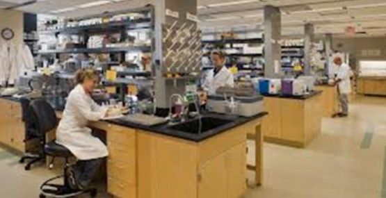 A woman in a lab coat is sitting at a desk in a lab.