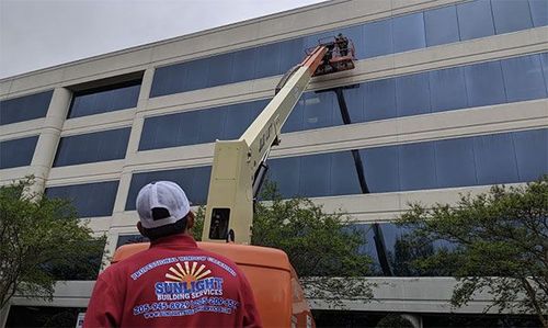 Worker in an orange vest on a lift cleaning windows of a modern office building