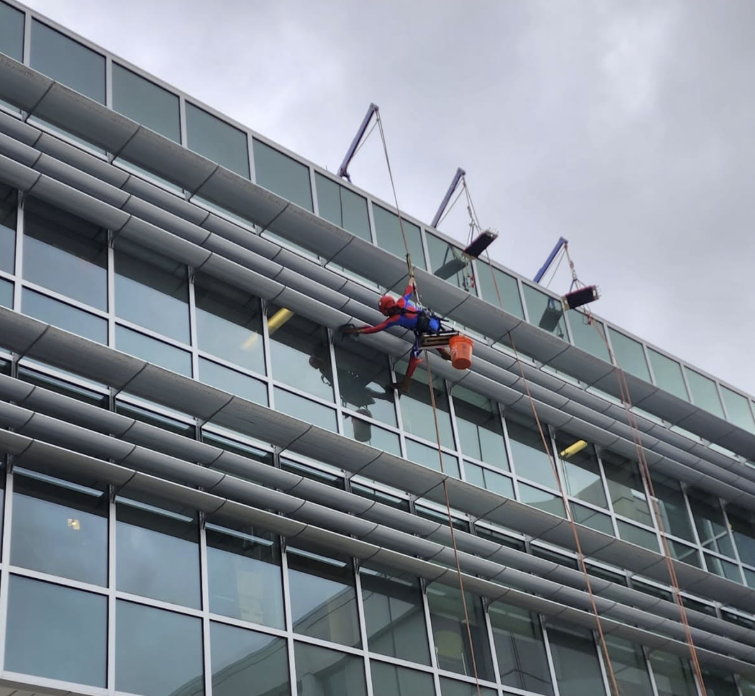 Worker suspended by ropes cleaning a glass office building facade