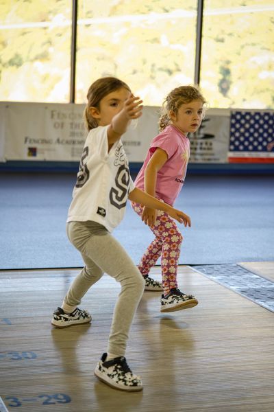 Two young children in athletic gear, one pointing, indoor setting.
