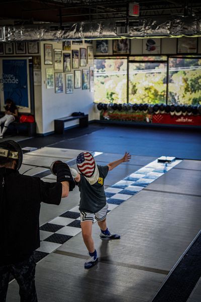 Two people in boxing gear sparring in a gym, one with an American flag face shield.