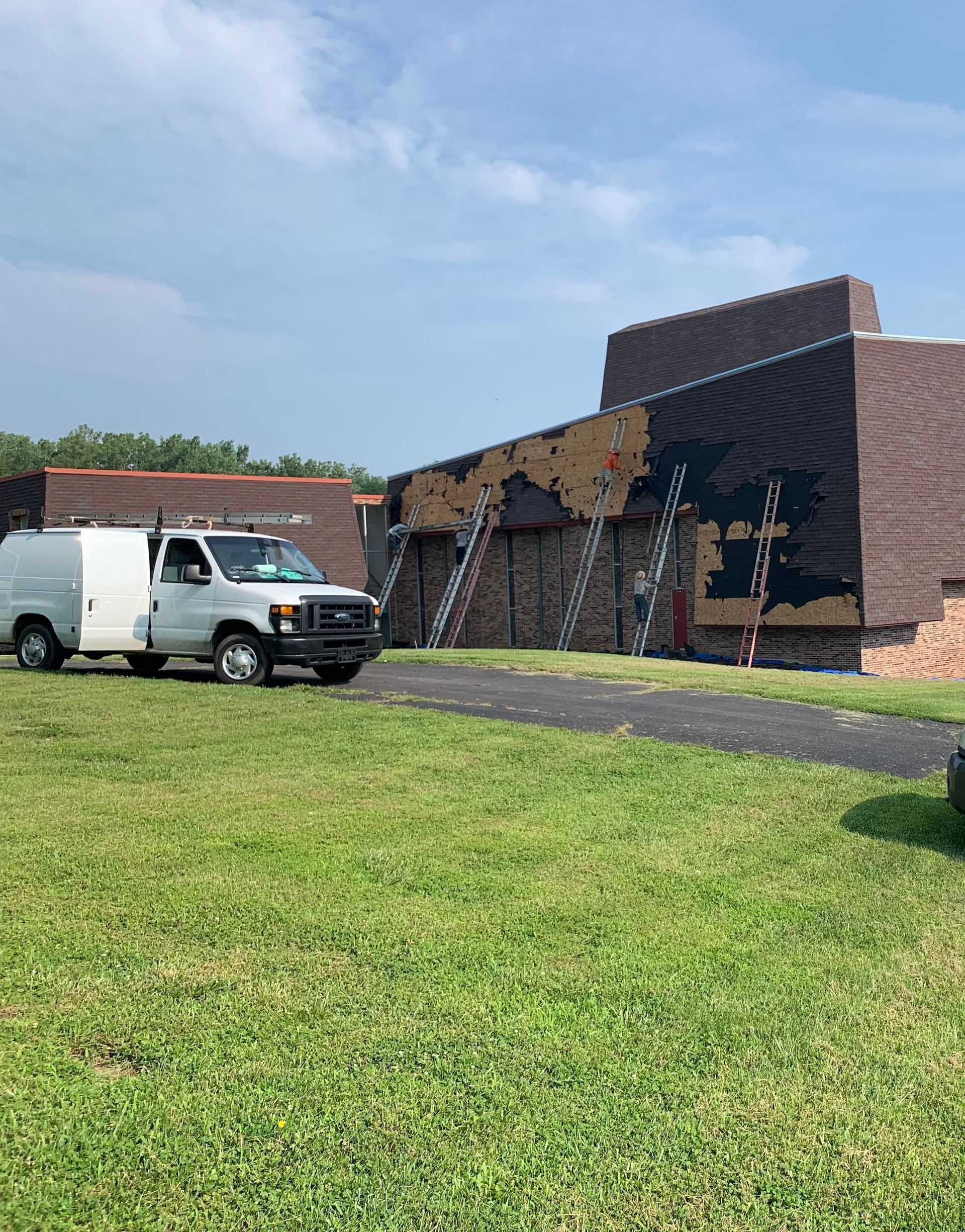 White work van parked on green grass; building being worked on. Ladders against the building. Sky is blue.
