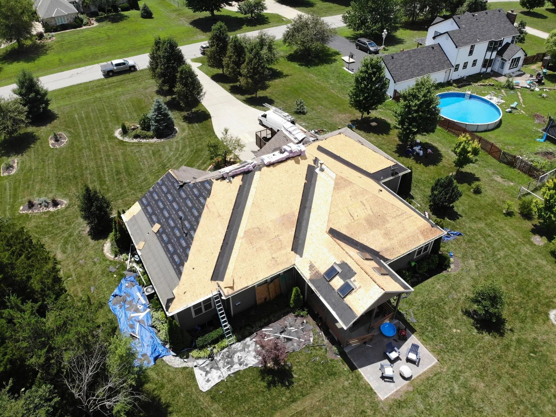 Aerial view of a house with a partially replaced roof. A swimming pool and surrounding yard are visible.