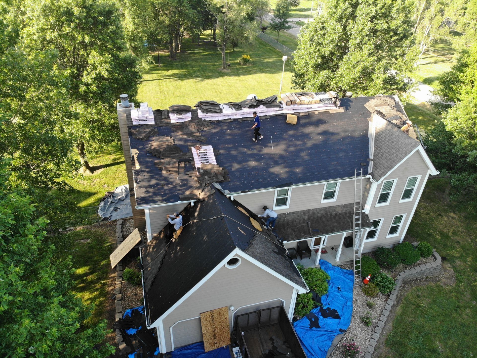 Overhead view of a house with roof replacement in progress; workers on the roof surrounded by materials.