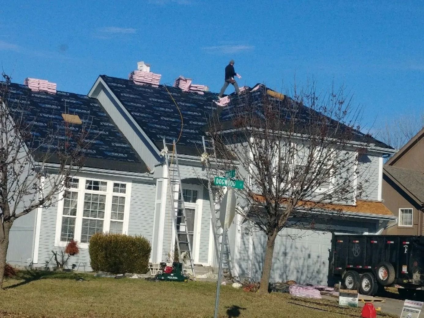 Roofers working on a residential home with bundles of shingles and a ladder.