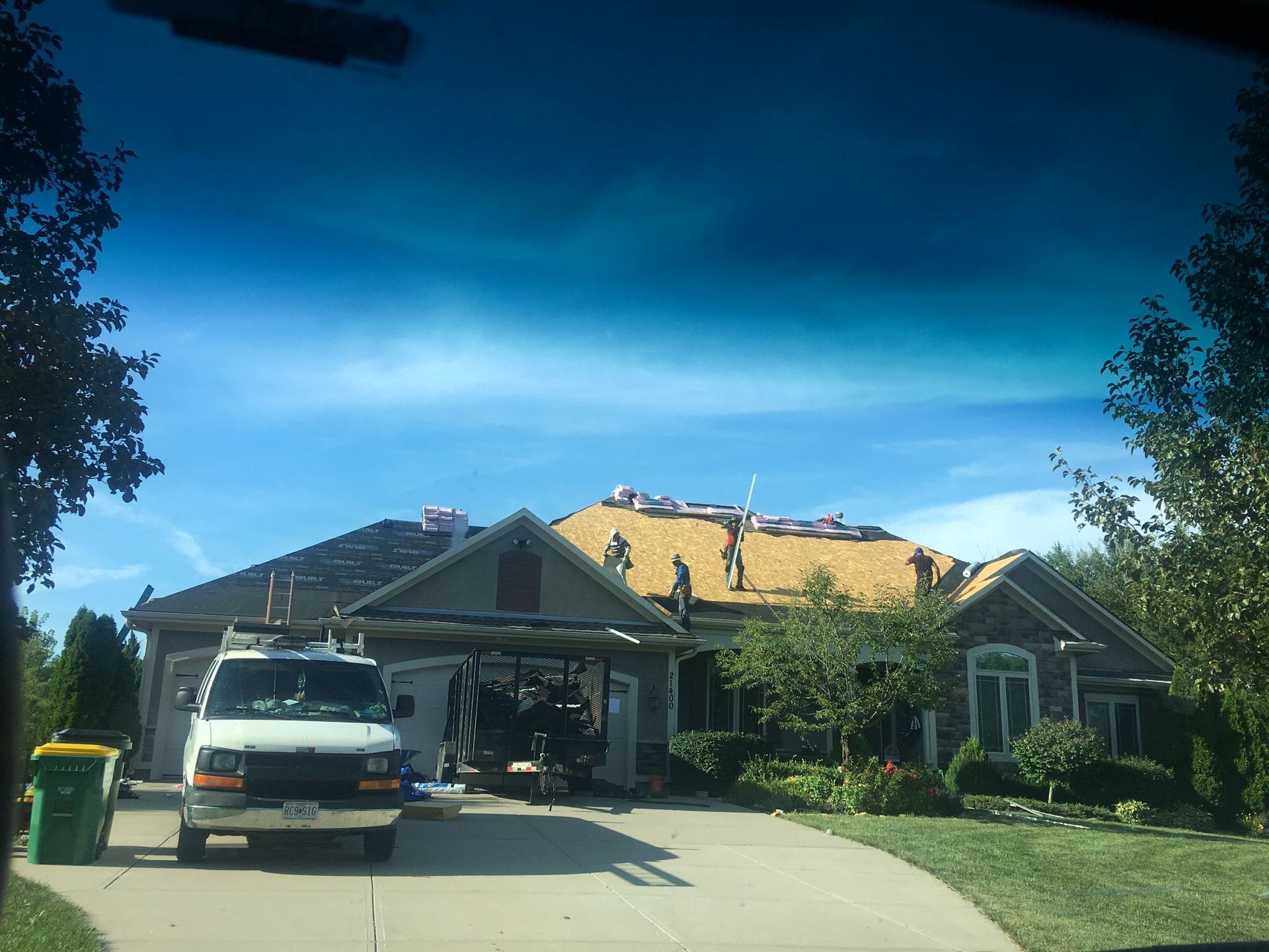 Roofers working on a house with a van parked in the driveway on a sunny day.