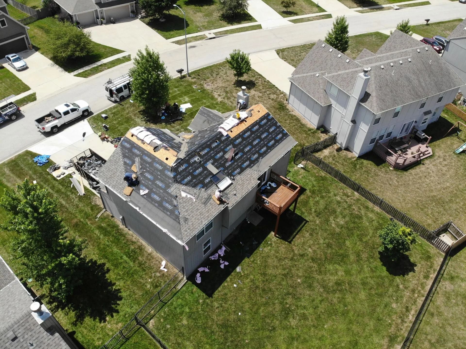 Aerial view of a house being re-roofed; a truck and workers are present.