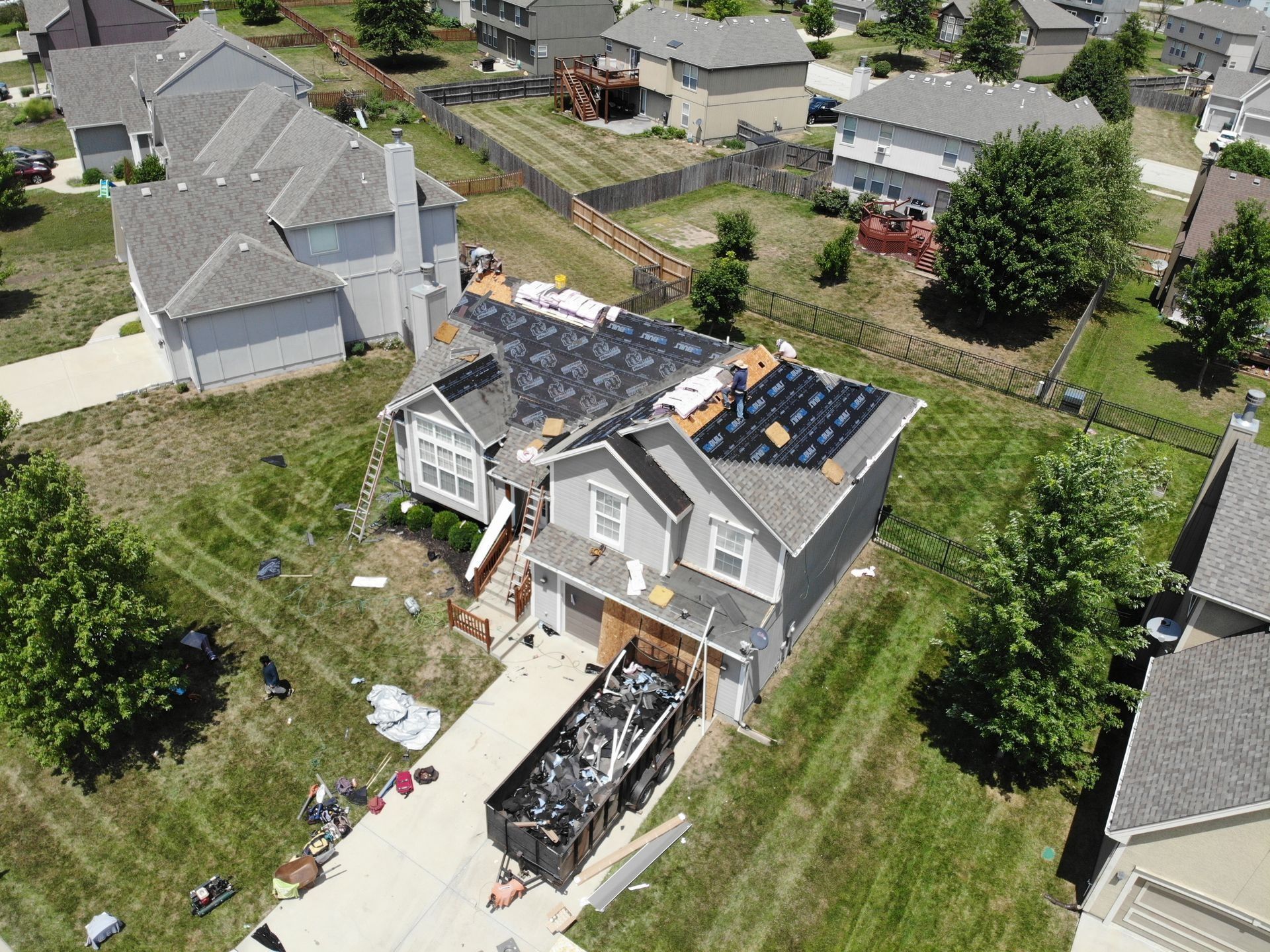 Aerial view of house under roof repair with a dumpster in the driveway.