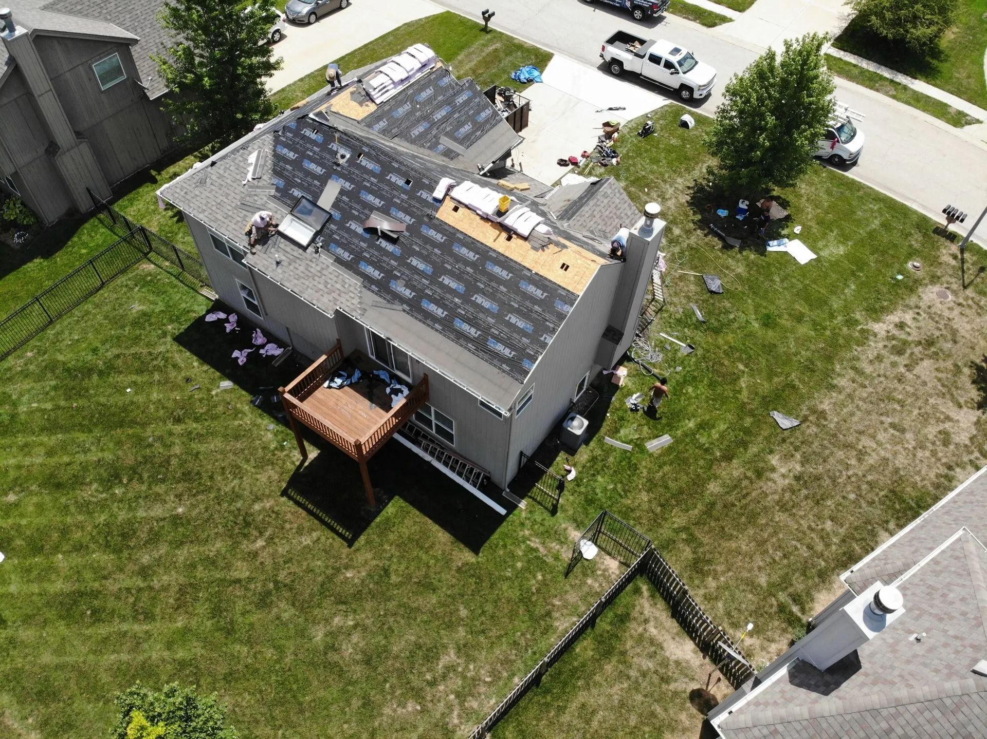 Aerial view of a house with roofing being replaced; workers on the roof, materials scattered, sunny day.