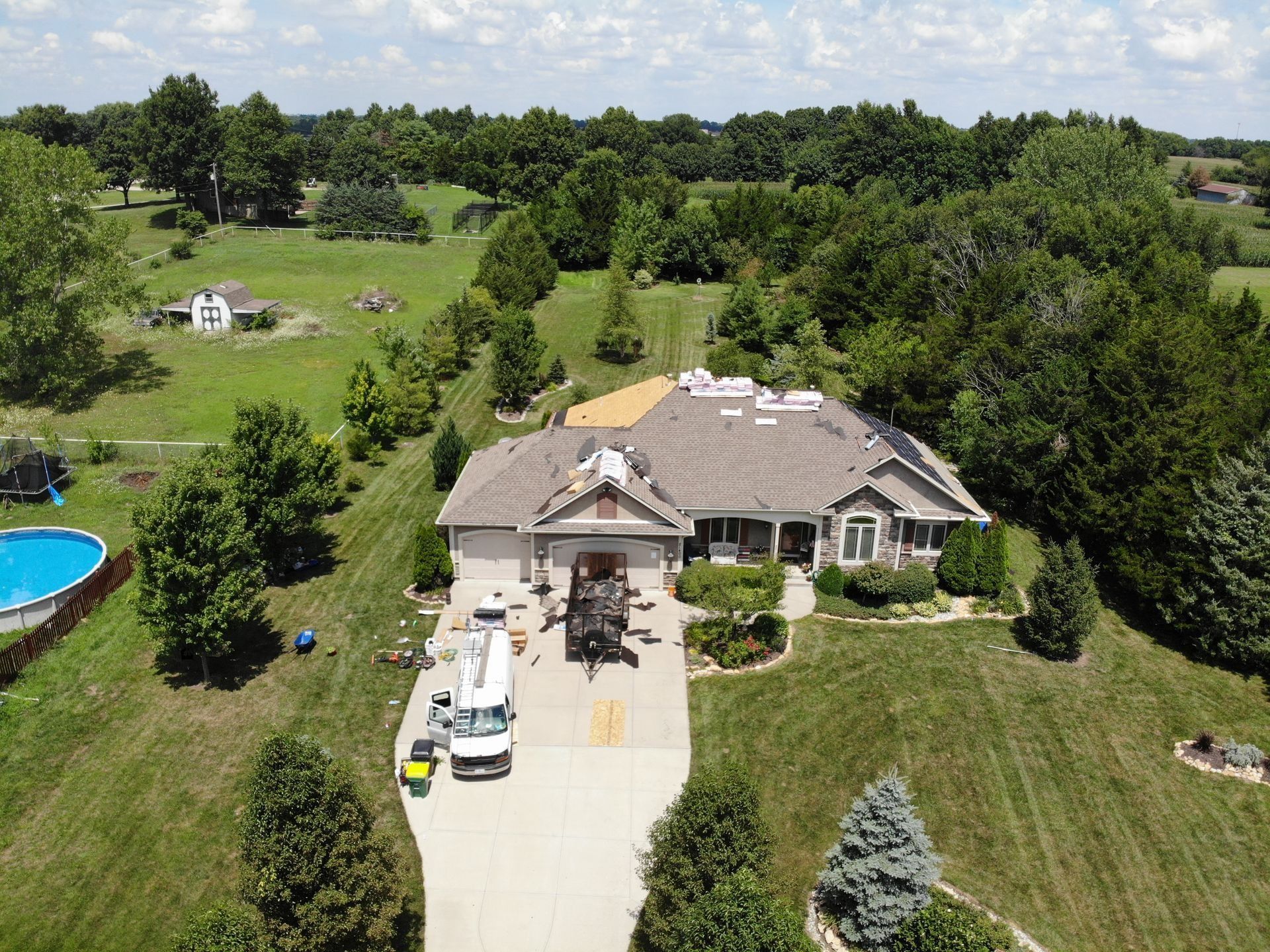 Aerial view of a house with roof replacement in progress; a truck and equipment are in the driveway.