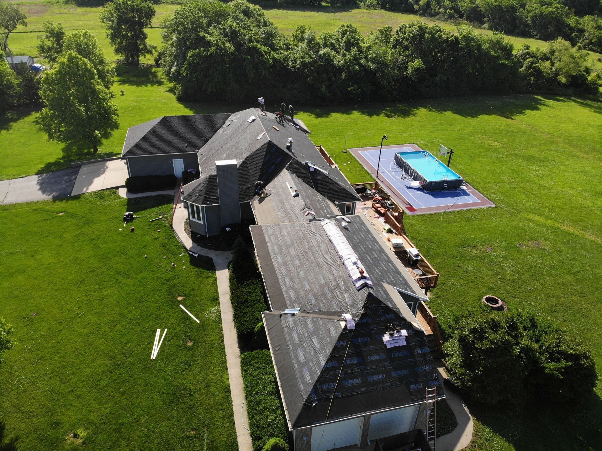 Aerial view of a house with a dark roof and a pool in a grassy field.
