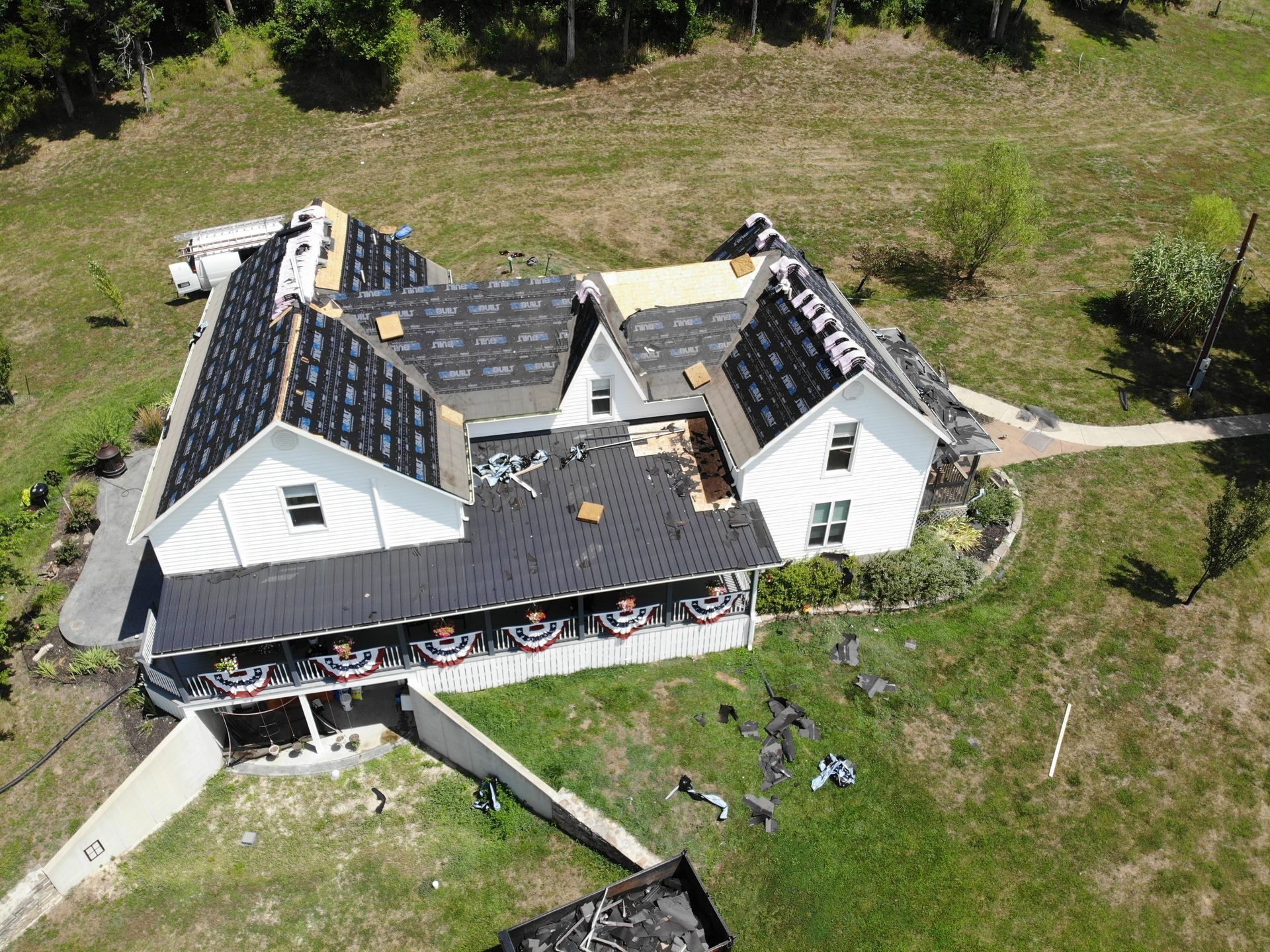 Aerial view of a house roof undergoing repair; black roofing material is installed, other sections exposed.