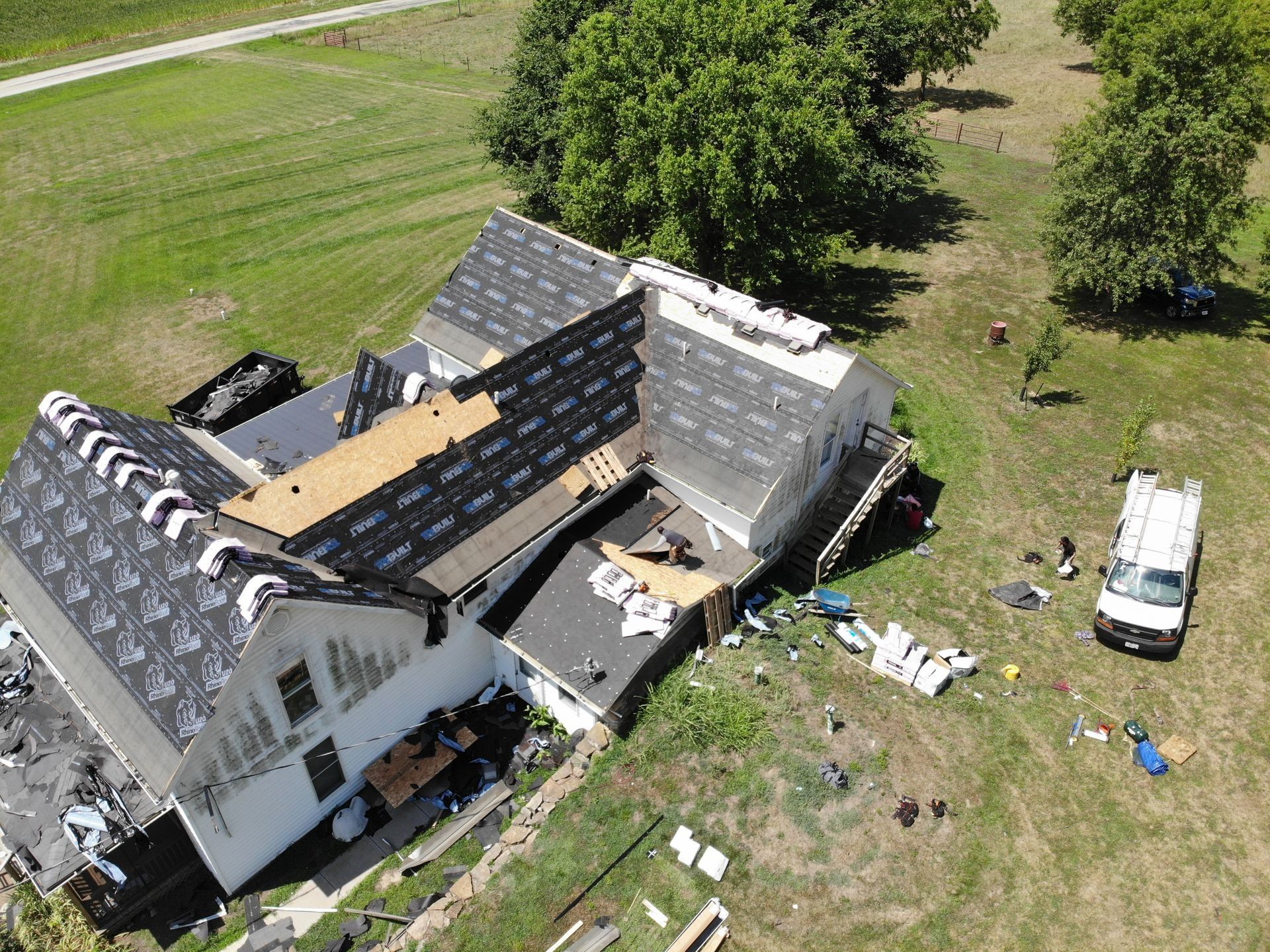 Overhead view of a house with roofing in progress; workers on the roof, material and truck present.