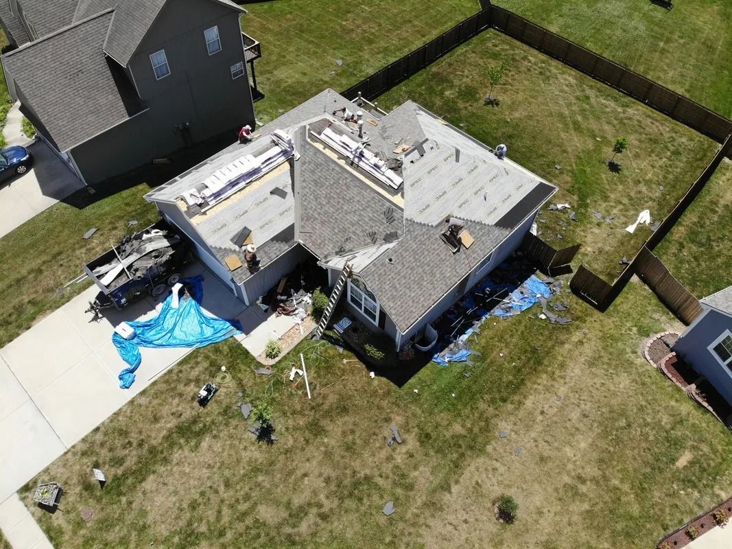 Aerial view of a house with sections of roof missing and covered by tarps. Debris is scattered around.