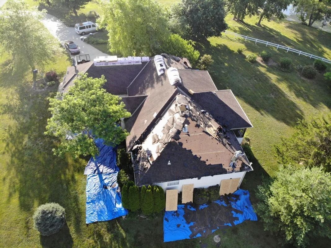 Aerial view of a house with significant roof damage, covered with blue tarps.