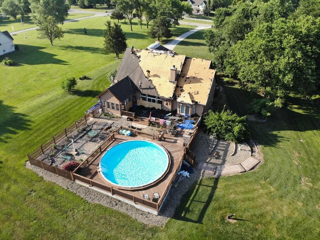 Aerial view of a house with a pool in the backyard, green lawn surrounding. Roof under construction.