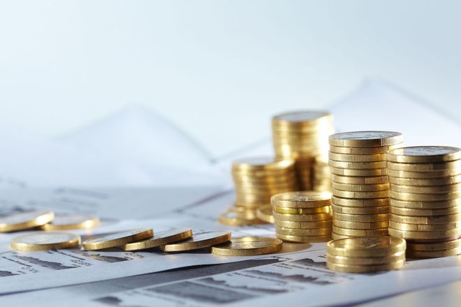 Stacks of gold coins on financial documents with a calculator in the background