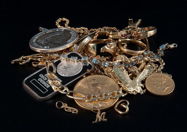Assortment of gold and silver jewelry and medals piled on a black background