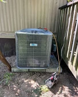 Outdoor air conditioner unit beside a mobile home wall, with a corded power tool on the ground.