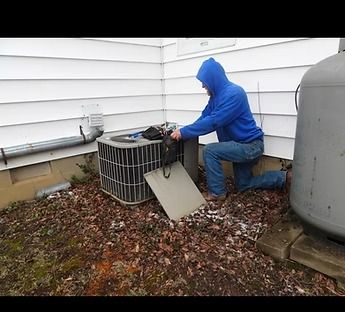 Worker in blue hoodie servicing an outdoor HVAC unit beside a house