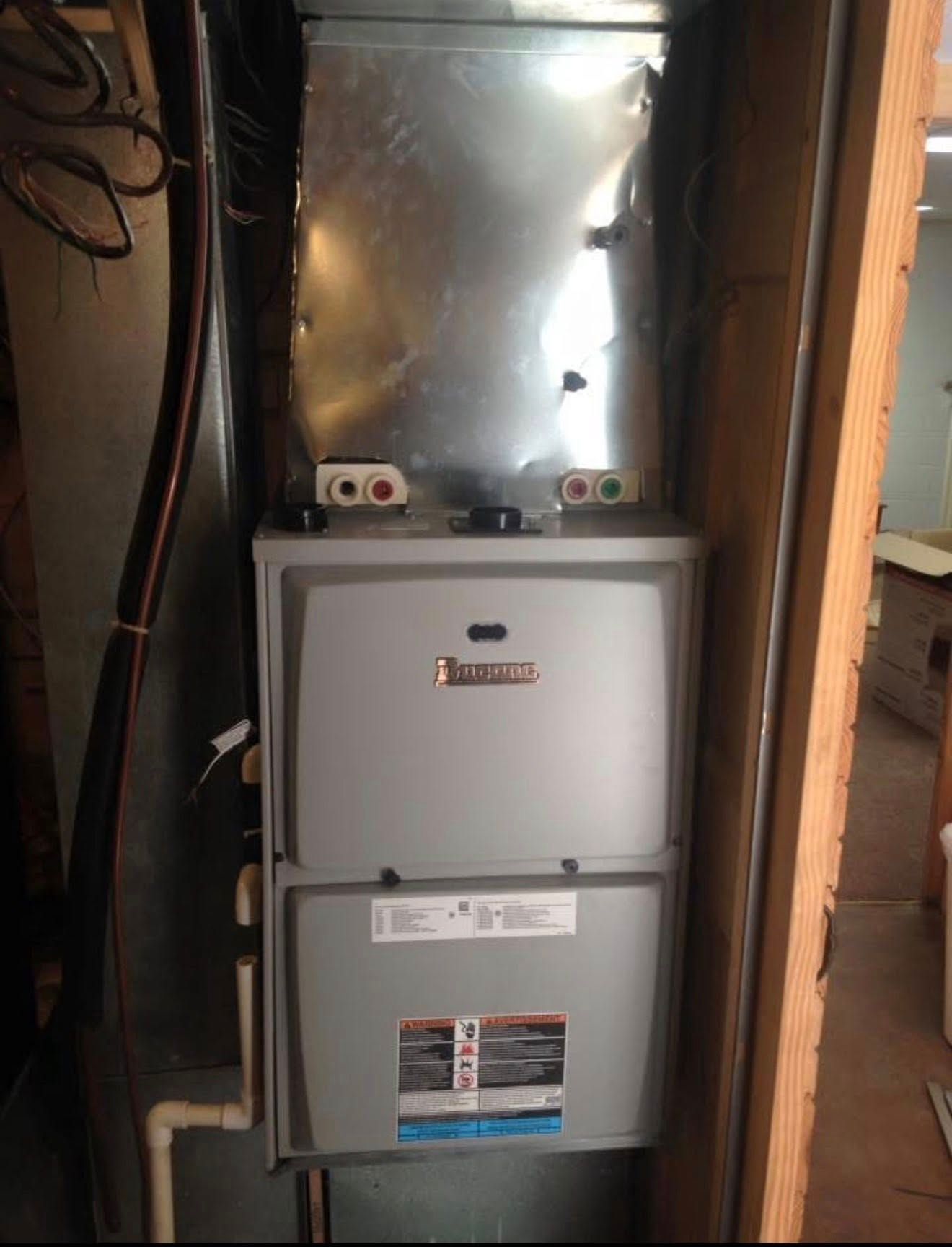 Two stacked gray furnace units in a narrow utility closet, with metal ductwork above.