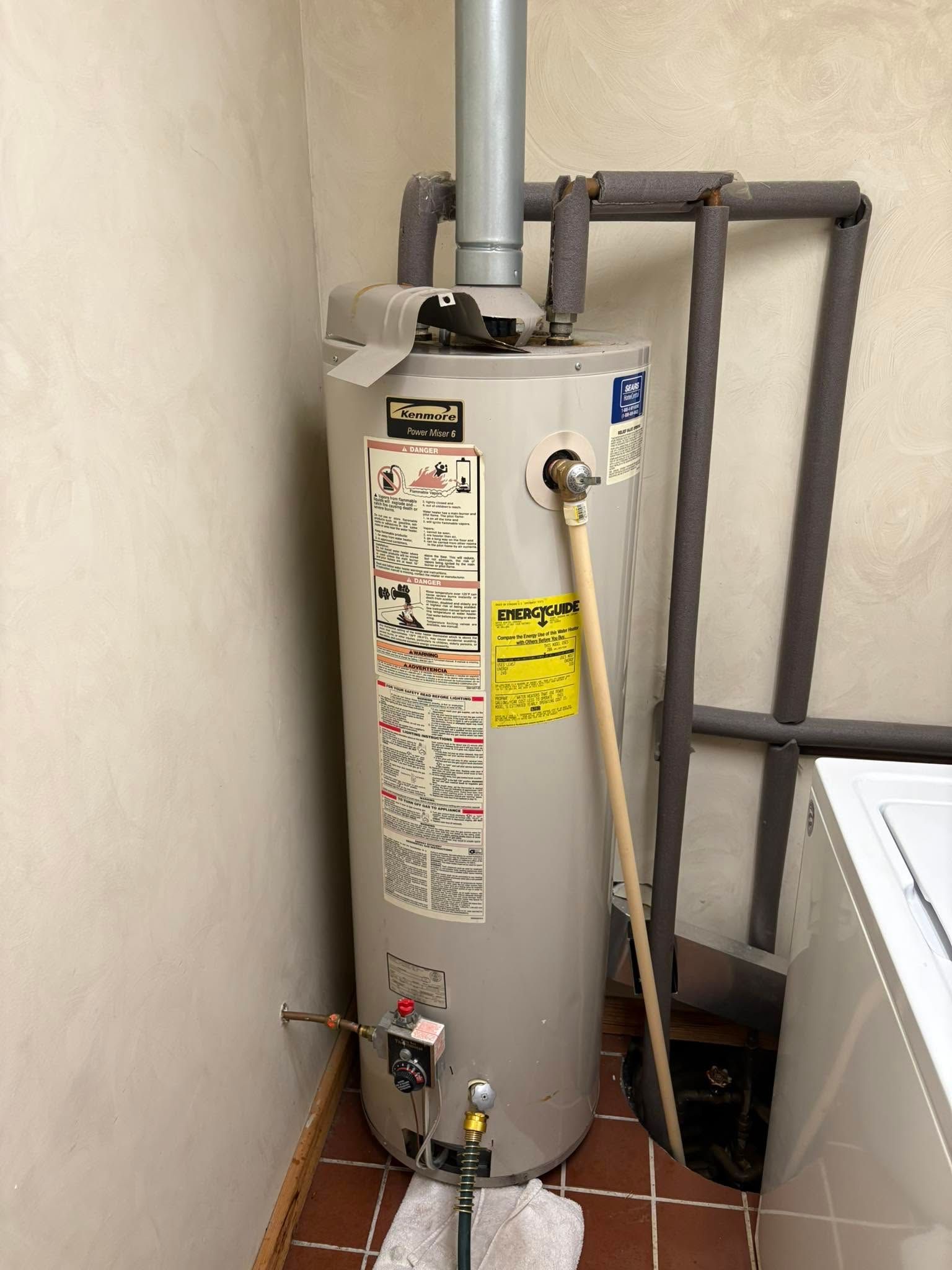 Water heater in a utility room with exposed pipes and a yellow gas line.