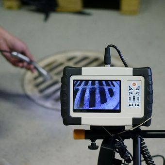 A man is using a camera to look at a manhole cover.