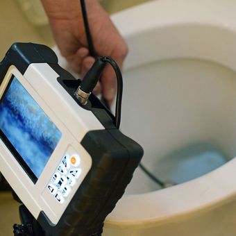 A person is holding a camera in front of a toilet.