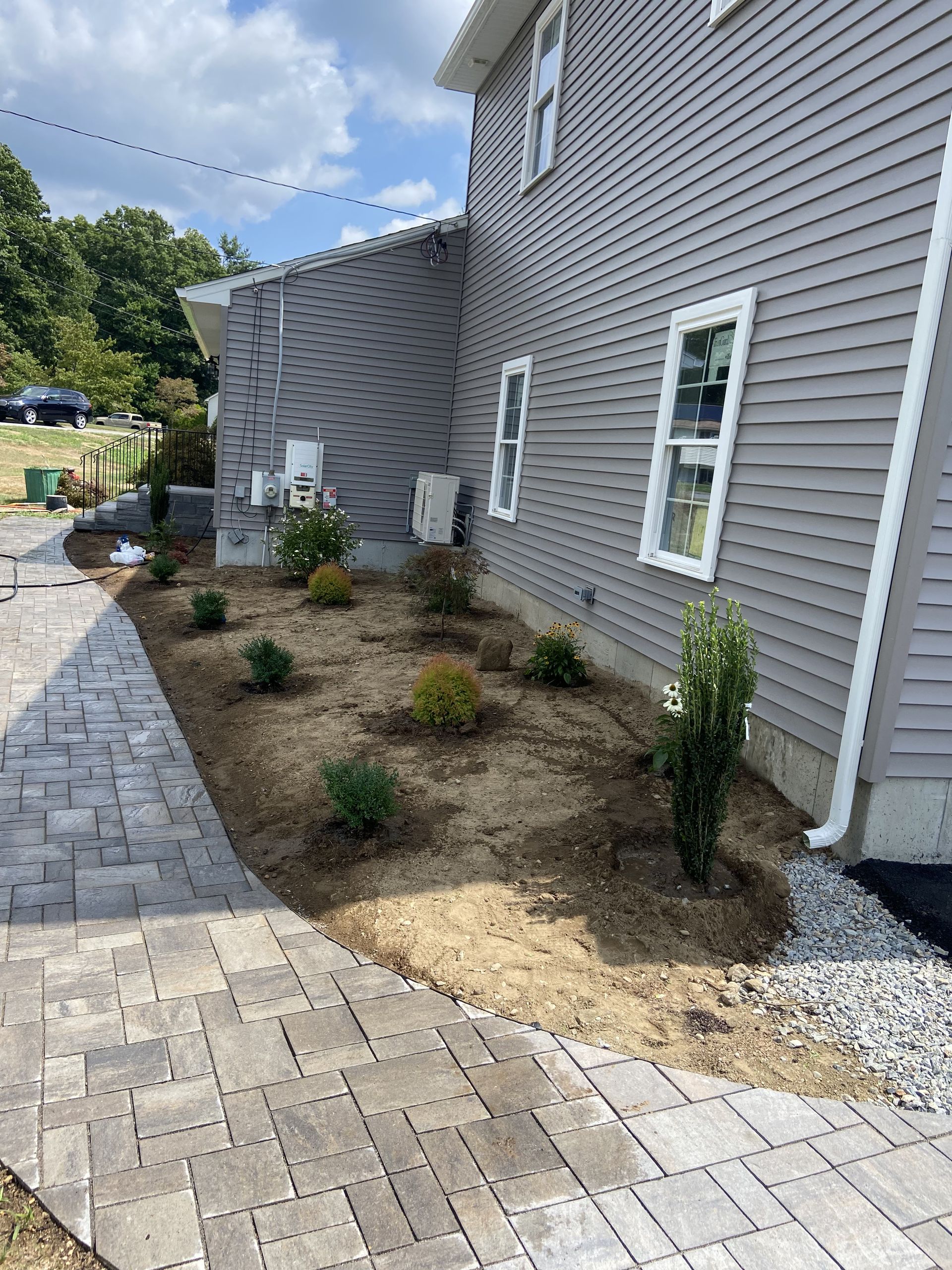 Side view of a house with new landscaping and a brick pathway.