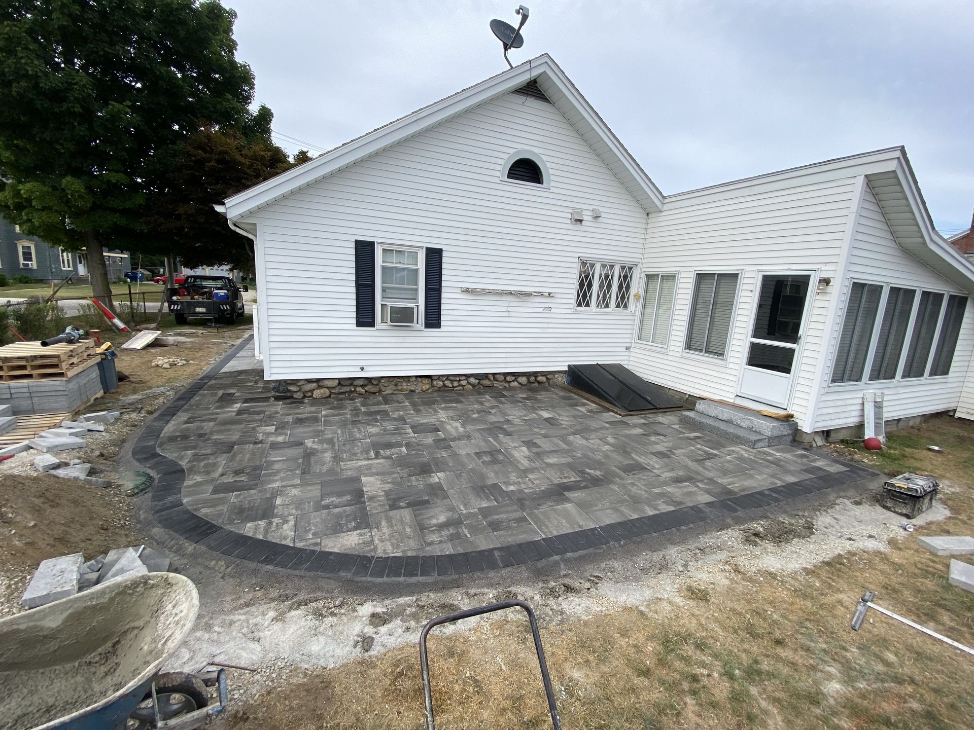 A newly built patio with dark gray pavers next to a white house.