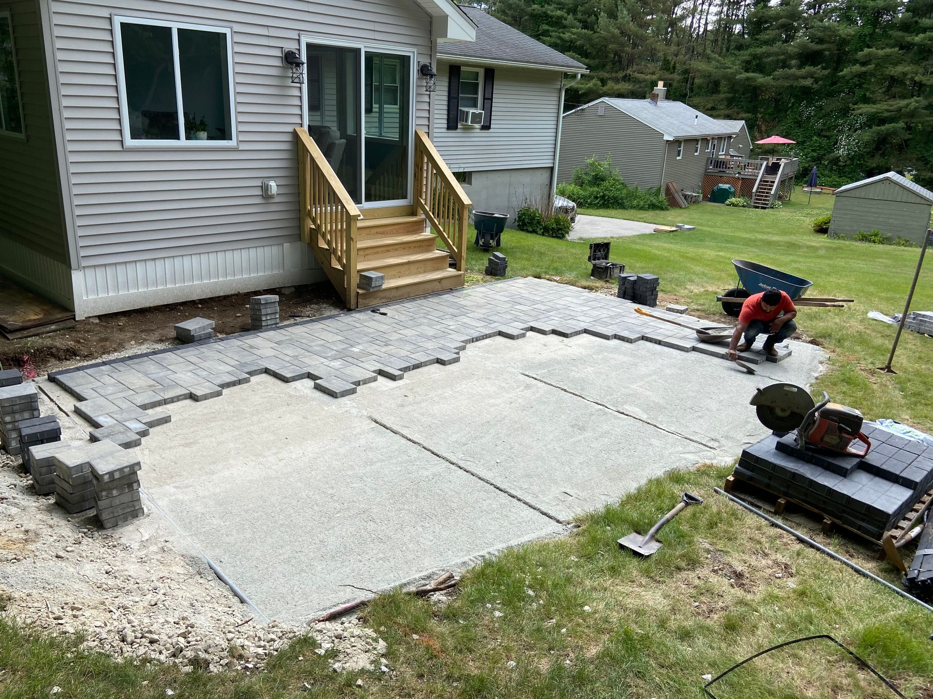 Construction of a concrete patio with pavers, next to a house with a sliding door.