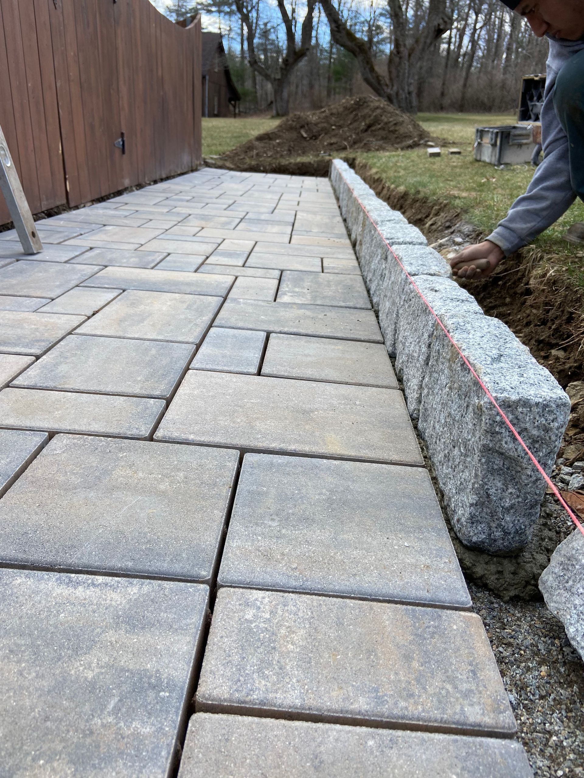 Person laying gray pavers for a patio, with a retaining wall being built.