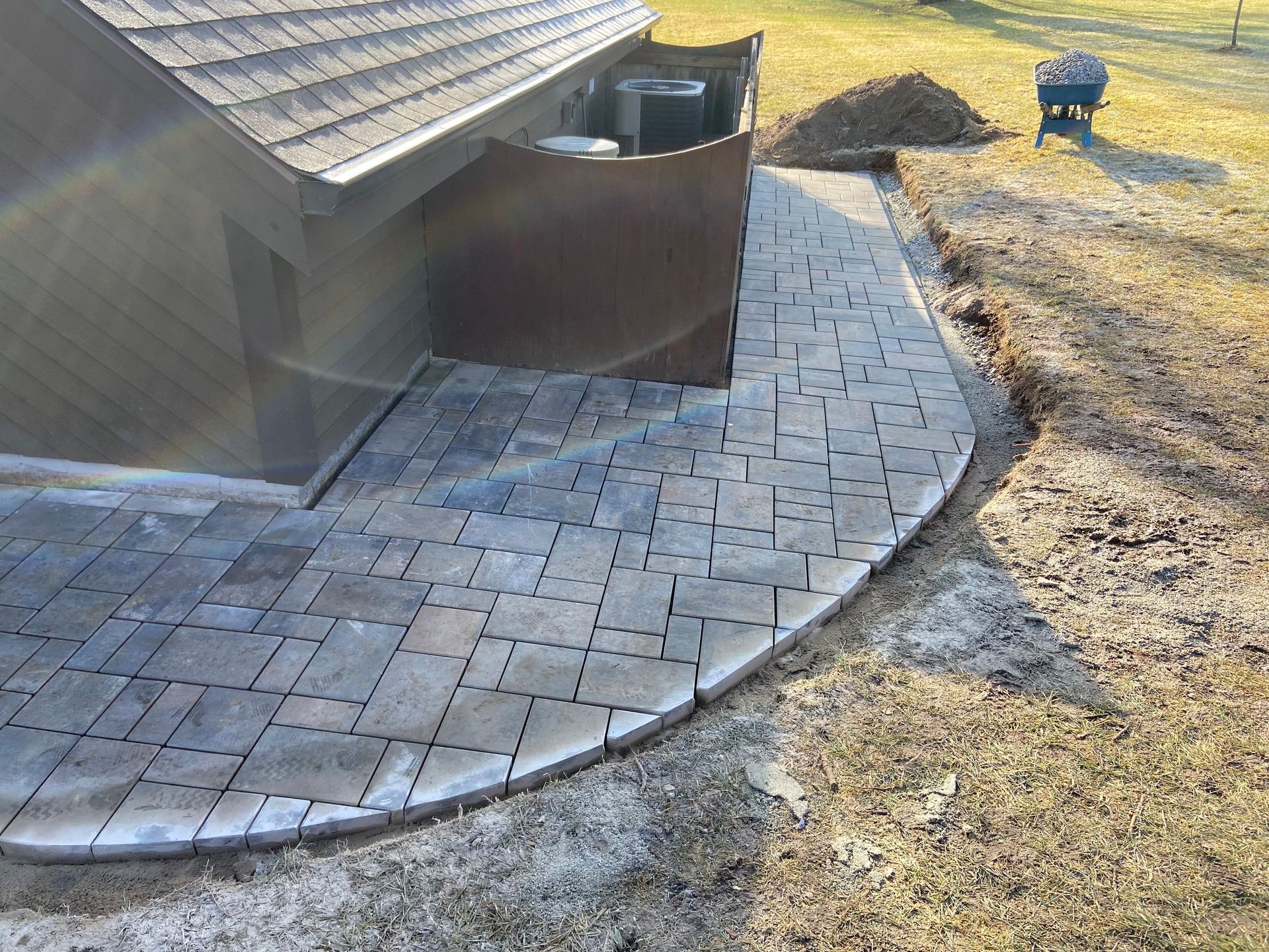 Brick patio curves along the side of a house; an air conditioning unit is next to the house.