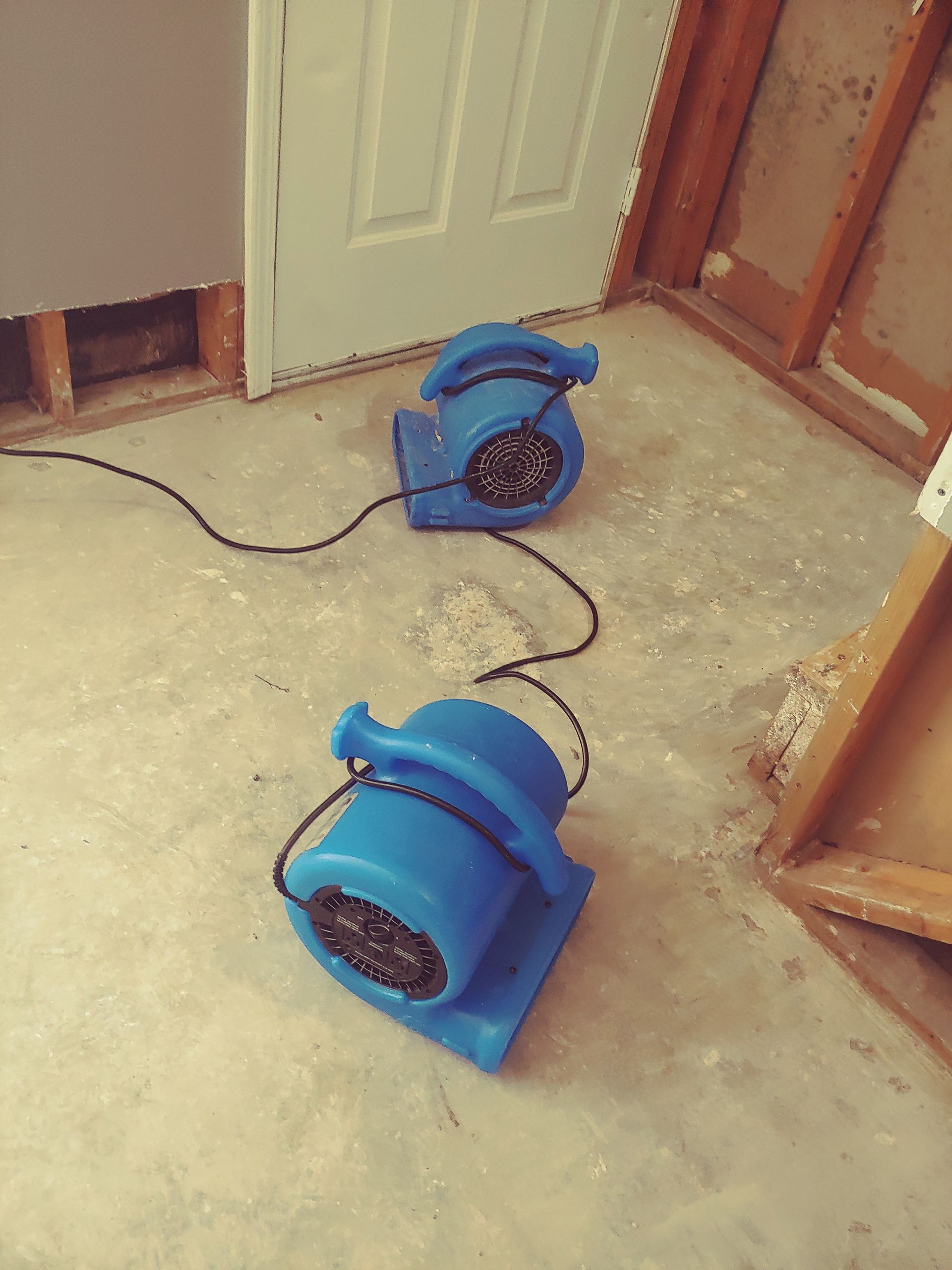 Two blue air movers on concrete floor drying a flooded room.